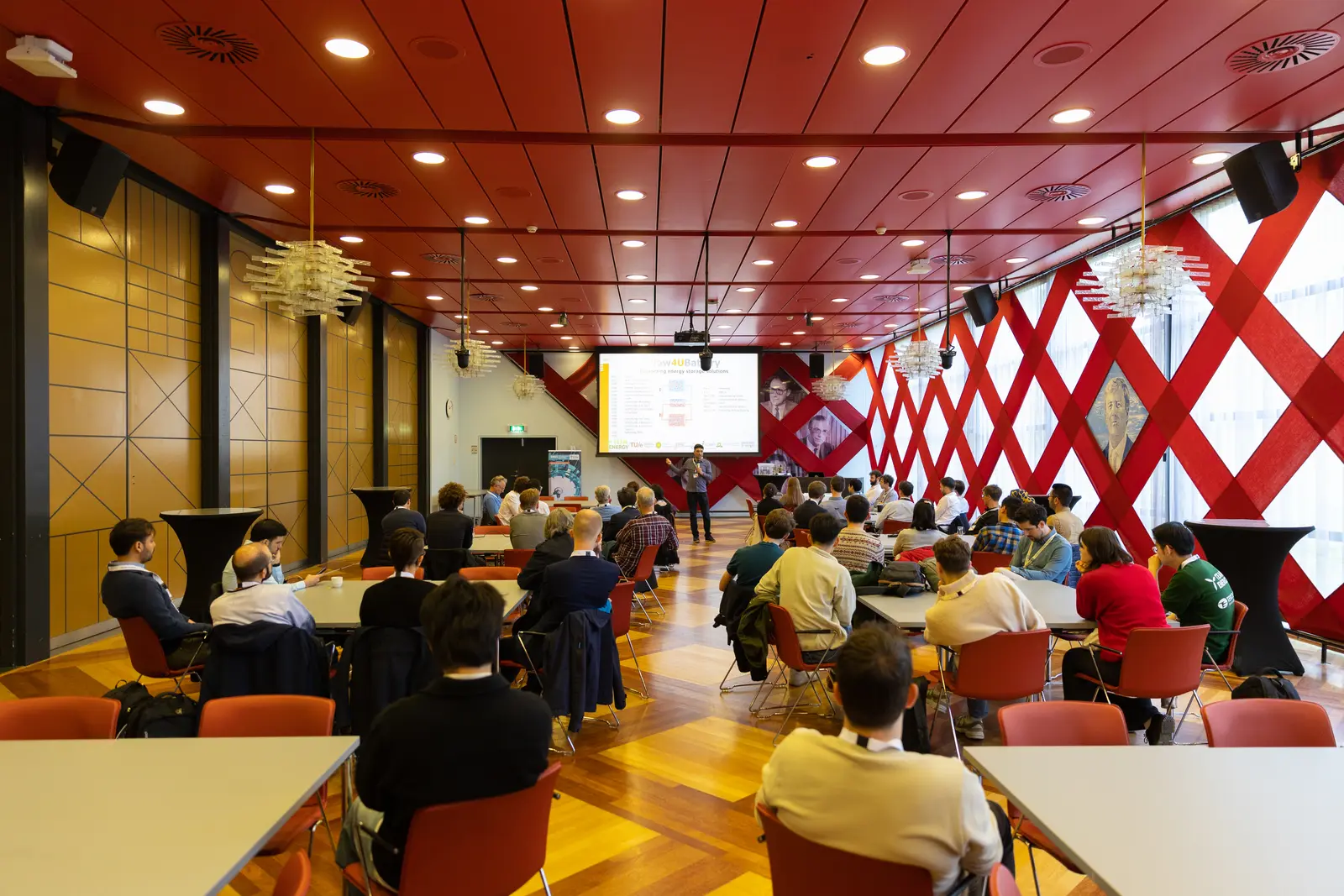 A conference room full of seated attendees with one person at the front addressing the room