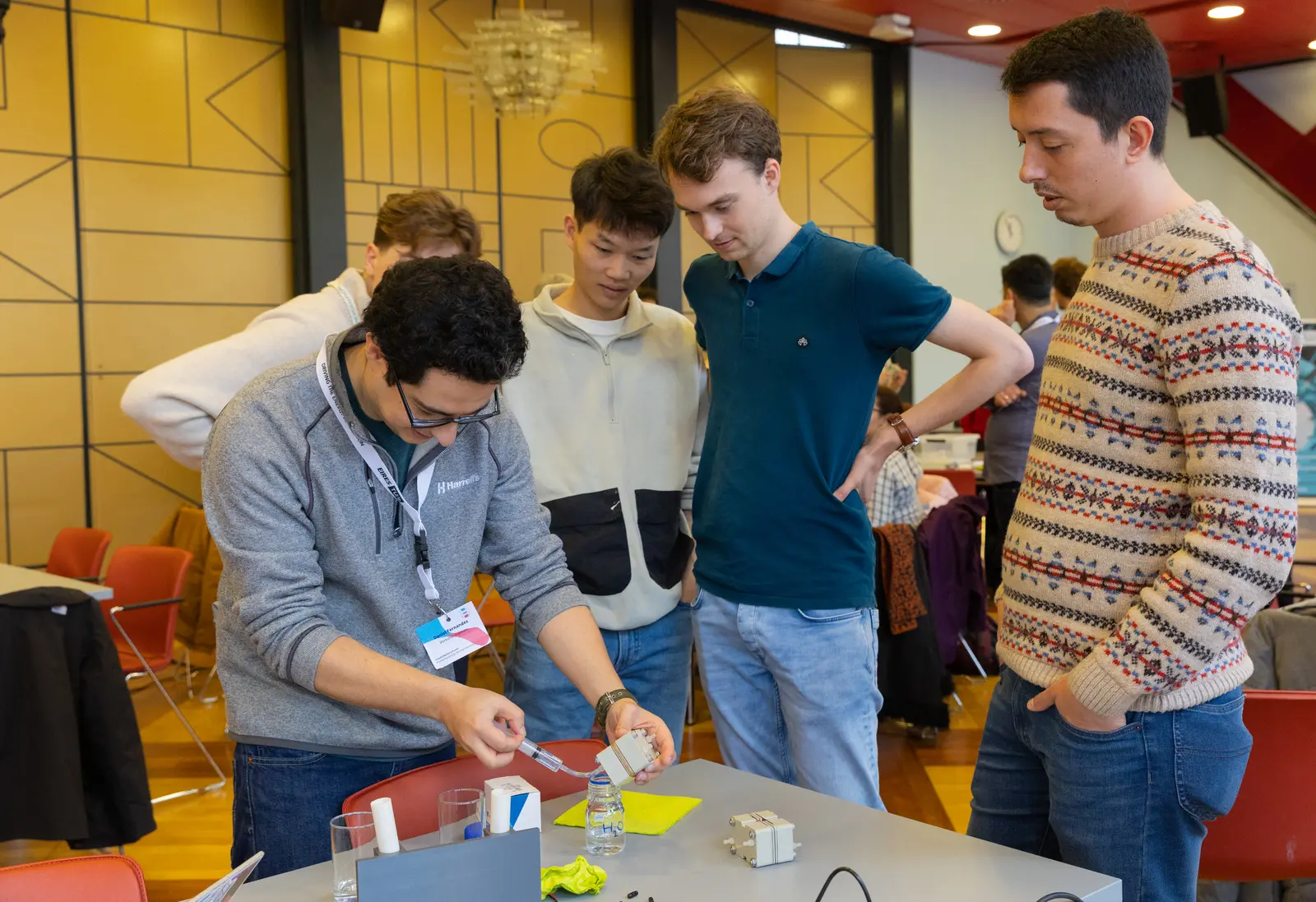 A group of people watching an individual pump water with a syringe through an assembled flow cell